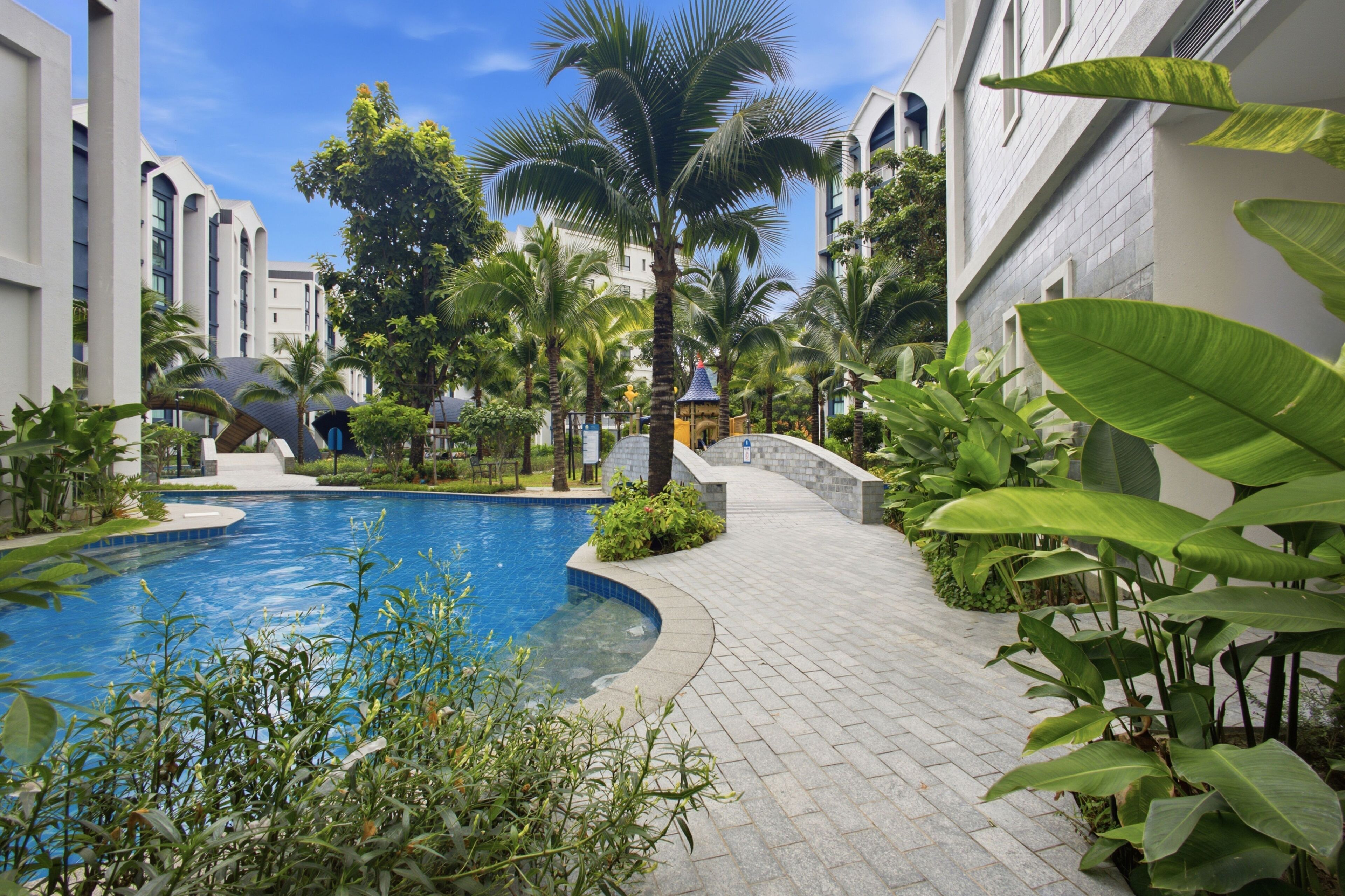 A swimming pool surrounded by lush greenery and modern buildings.