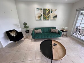 A modern living room with a green sofa, a black armchair, a coffee table, and abstract wall art. - Stylish, modern, centrally-located home, 5 mins away from key amenities. (Diego Martin Regional Corporation)