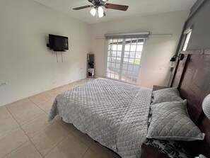 A bedroom with a bed, a ceiling fan, a TV mounted on the wall, a window with blinds, and a door with a mirror. - Stylish, modern, centrally-located home, 5 mins away from key amenities. (Diego Martin Regional Corporation)