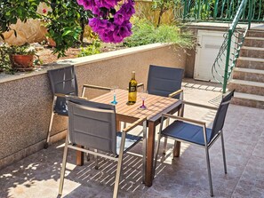 Un patio al aire libre con una mesa, sillas, una botella de vino y una planta en maceta.