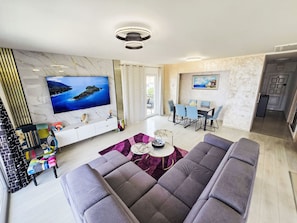 A modern living room with a large flat-screen TV, a sofa set, a dining area with chairs, and a kitchen in the background. - Lux Adriatica 3 by Interhome (Trogir/Okrug Gornji)