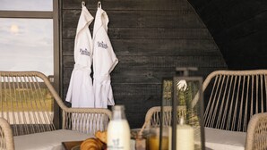 A room with wicker chairs, a table with a tray of croissants, a bottle of milk, and two white robes hanging on a wooden wall. - THE HOG HUT, luxury holiday cottage, with hot tub in Llanarth (Llanarth)