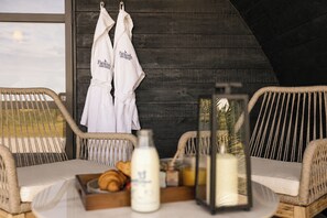 A room with wicker chairs, a table with a tray of croissants, a bottle of milk, and two white robes hanging on a wooden wall. - THE HOG HUT, luxury holiday cottage, with hot tub in Llanarth (Llanarth)