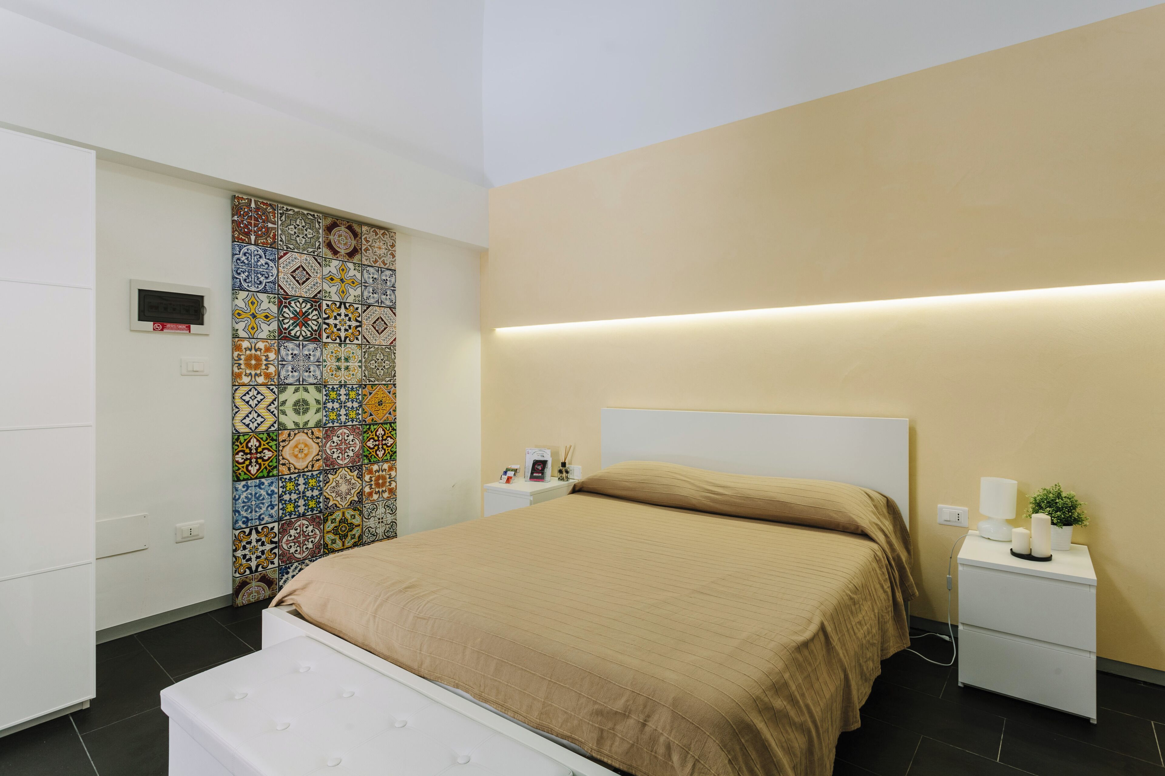 Une chambre à coucher moderne avec un grand lit, une table de chevet avec une lampe et un mur recouvert de carreaux colorés.