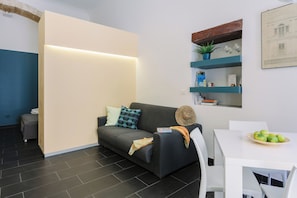 A modern living room with a sofa, a dining table, and a kitchen area. - 1743LOft Studio Alla Corte (Siracusa)