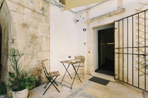 A small outdoor seating area with a table and chairs, a potted plant, and a metal gate. - 1743LOft Studio Alla Corte (Siracusa)