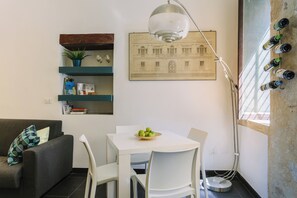 A modern living space with a dining area, a sofa, a white table, and a wall-mounted wine rack. - 1743LOft Studio Alla Corte (Siracusa)