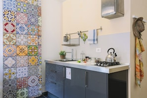 A kitchen with a tiled backsplash, a stainless steel sink, a kettle, and a hanging towel rack. - 1743LOft Studio Alla Corte (Siracusa)