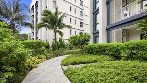 A pathway leading to a modern building with multiple floors, surrounded by lush greenery and palm trees. - Spacious 2BR at The Title Halo • Walk to Nai Yang Beach (Tambon Sa Khu)