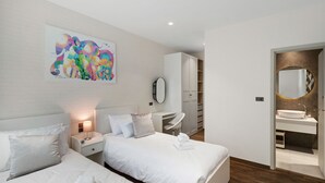 A hotel room with two beds, a nightstand, a bedside table, a desk, a chair, a wardrobe, a mirror, and a bathroom with a sink. - Spacious 2BR at The Title Halo • Walk to Nai Yang Beach (Tambon Sa Khu)