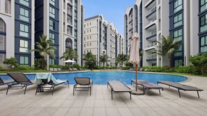 A swimming pool area with lounge chairs and palm trees. - Spacious 2BR at The Title Halo • Walk to Nai Yang Beach (Tambon Sa Khu)