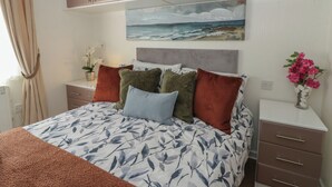 A bedroom with a bed, a nightstand, a painting, and a vase with flowers. - 73 CILDRAETH, pet friendly, country holiday cottage in Llanarth (New Quay)