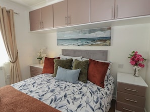 A bedroom with a bed, a nightstand, a painting, and a vase with flowers. - 73 CILDRAETH, pet friendly, country holiday cottage in Llanarth (New Quay)