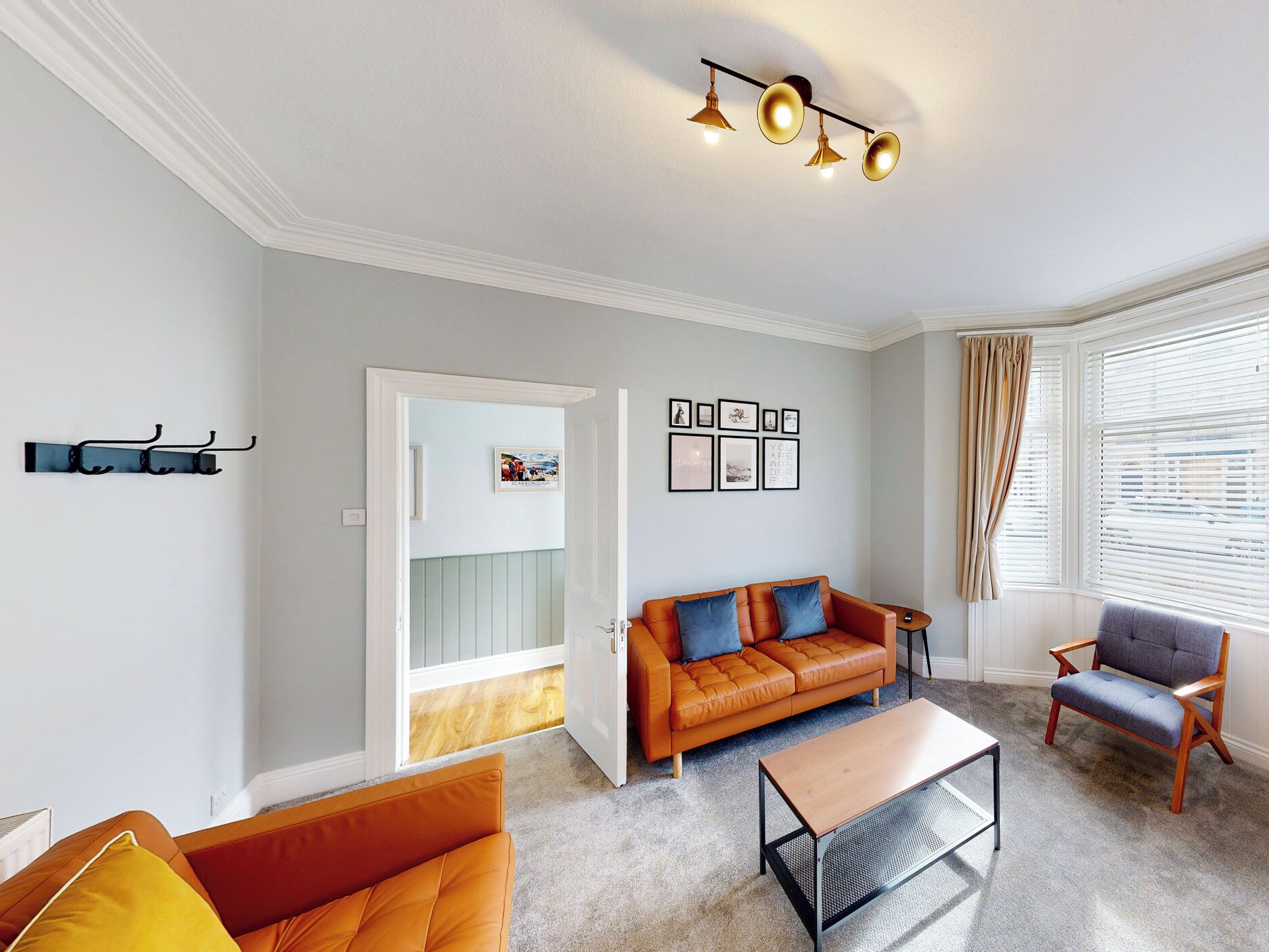 Ein Wohnzimmer mit einer Couch, einem Couchtisch und einem Sessel. Eine Tür führt in einen anderen Raum, und ein Fenster mit Vorhängen ist vorhanden.