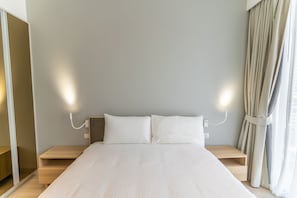 A neatly made bed with a headboard, bedside tables, and a wall-mounted light fixture. - Cassia Residences Spacious 2BR with Lagoon View (Choeng Thale (Thalang District))