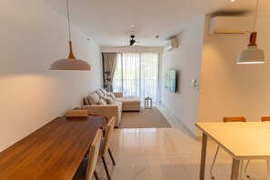 A modern living room with a wooden dining table, a sofa, and a TV mounted on the wall. - Cassia Residences Spacious 2BR with Lagoon View (Choeng Thale (Thalang District))