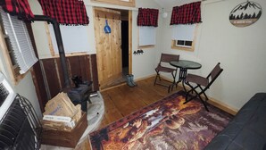 Una habitación acogedora con una puerta de madera, una mesa pequeña con sillas, un tapete estampado y un sofá negro.