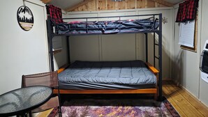 Habitación con literas, una mesita pequeña, una silla, un adorno en la pared y una ventana con cortinas.