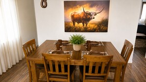 Un comedor con mesa y sillas de madera, una planta en maceta y un cuadro de un toro en la pared.