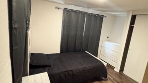 Una habitación pequeña con cama individual, piso de madera, cómoda blanca y cortina.