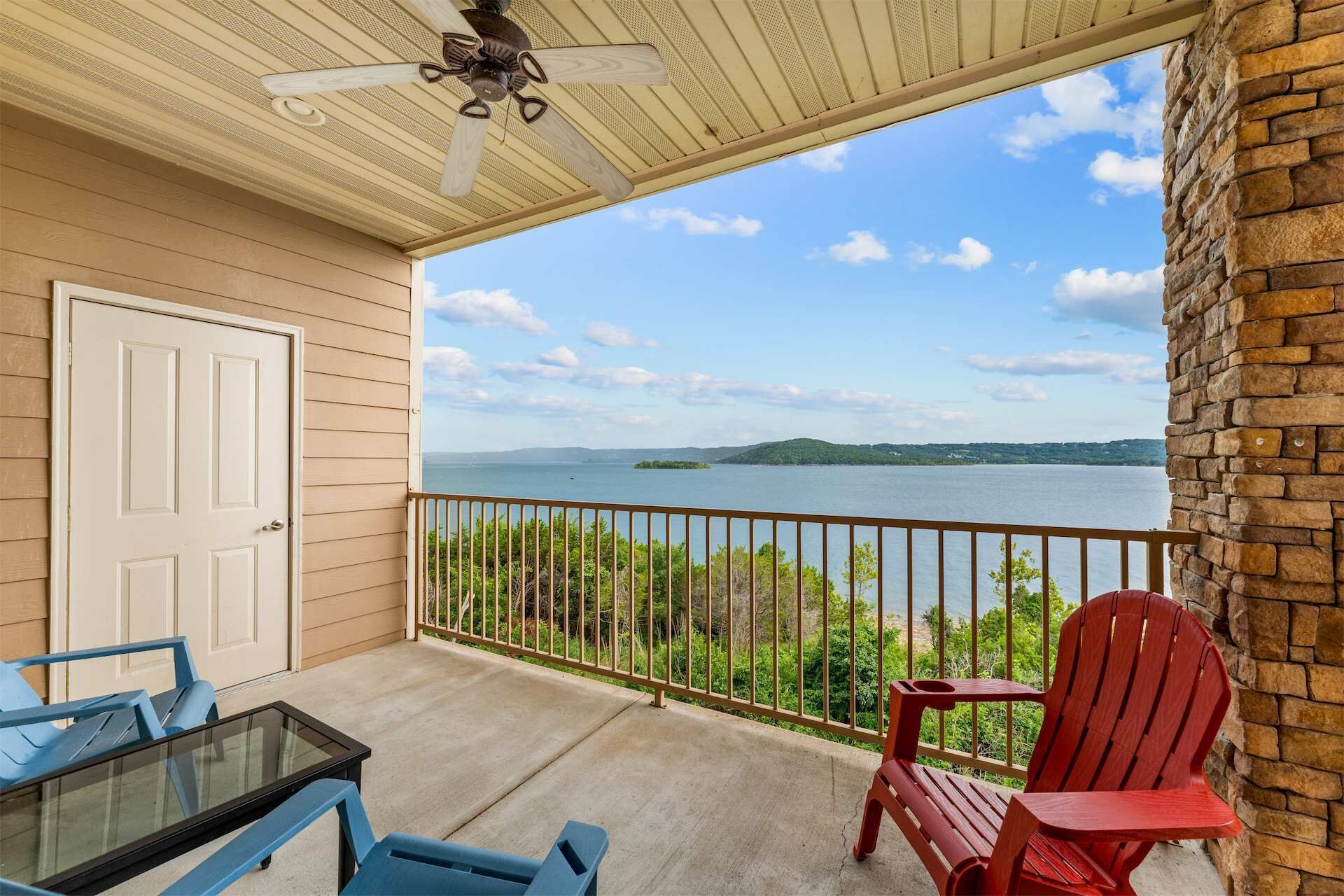 A balcony with a view of a lake, a ceiling fan, and a table with chairs.