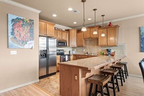 A modern kitchen with wooden cabinets, stainless steel appliances, a large island with bar stools, and pendant lighting. - Yakov's Hideaway - Lakefront (Hollister)