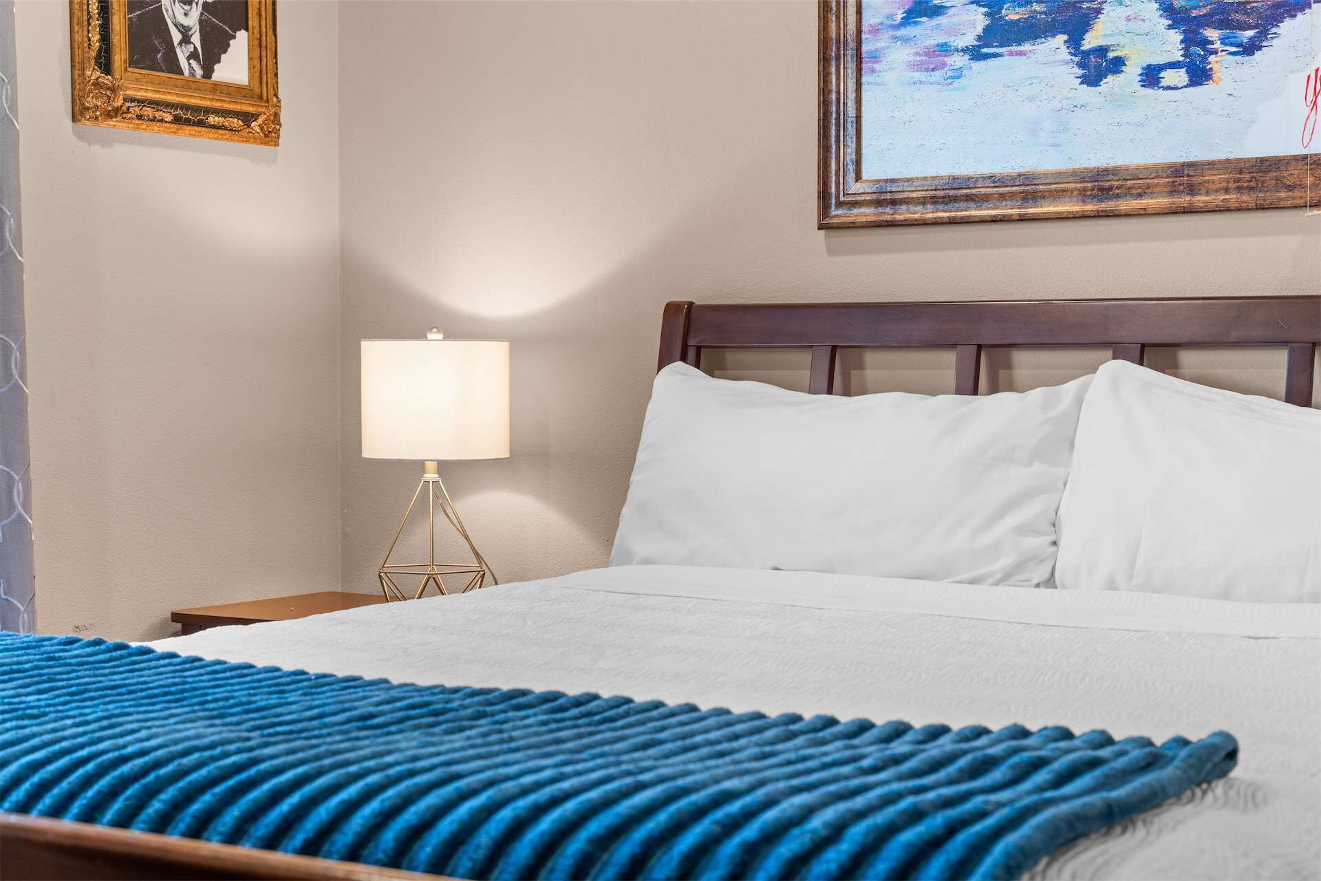 Una habitación de hotel con una cama, una mesita de noche con lámpara y un cuadro en la pared.