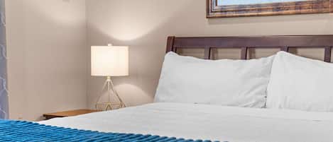 Una habitación de hotel con una cama, una mesita de noche con lámpara y un cuadro en la pared.