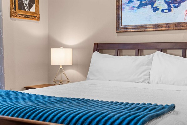 Una habitación de hotel con una cama, una mesita de noche con lámpara y un cuadro en la pared.