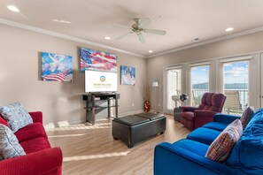 A spacious living room with a red and blue sofa set, a black ottoman, and a ceiling fan. - Yakov's Retreat - Pool Access (Hollister)