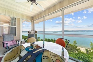 Une pièce dotée d’une grande fenêtre donnant sur un plan d’eau, d’un ventilateur de plafond et d’une table avec des chaises.
