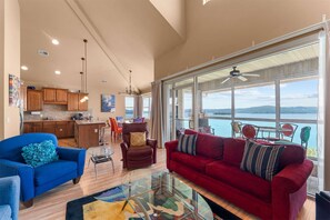 A spacious living area with a red sofa, a blue armchair, and a glass coffee table. There is a kitchen area with wooden cabinets and a dining space with a table and chairs. - The Smirnoff Suite - 3bdr (Hollister)