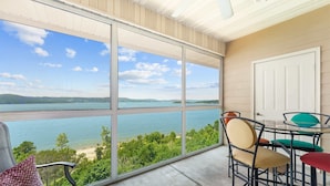 Uma varanda com vista para um lago e colinas, mobiliada com cadeiras e uma mesa.