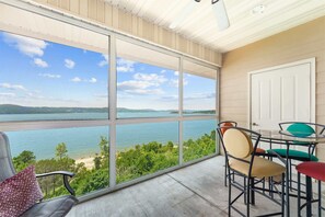 Ein Balkon mit Blick auf einen See und Hügel, ausgestattet mit Stühlen und einem Tisch.