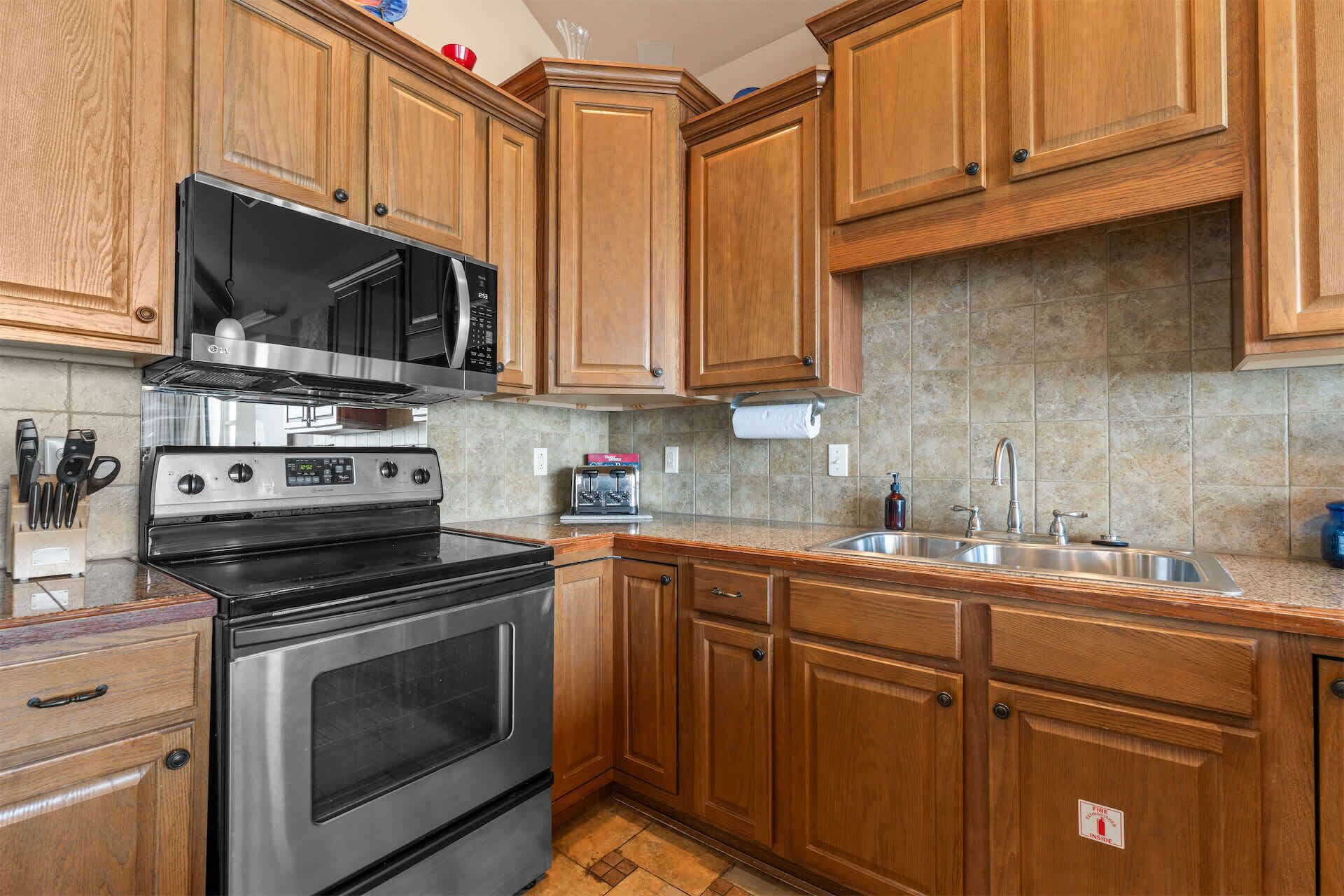 A kitchen with wooden cabinets, a stainless steel stove, a microwave, and a sink.