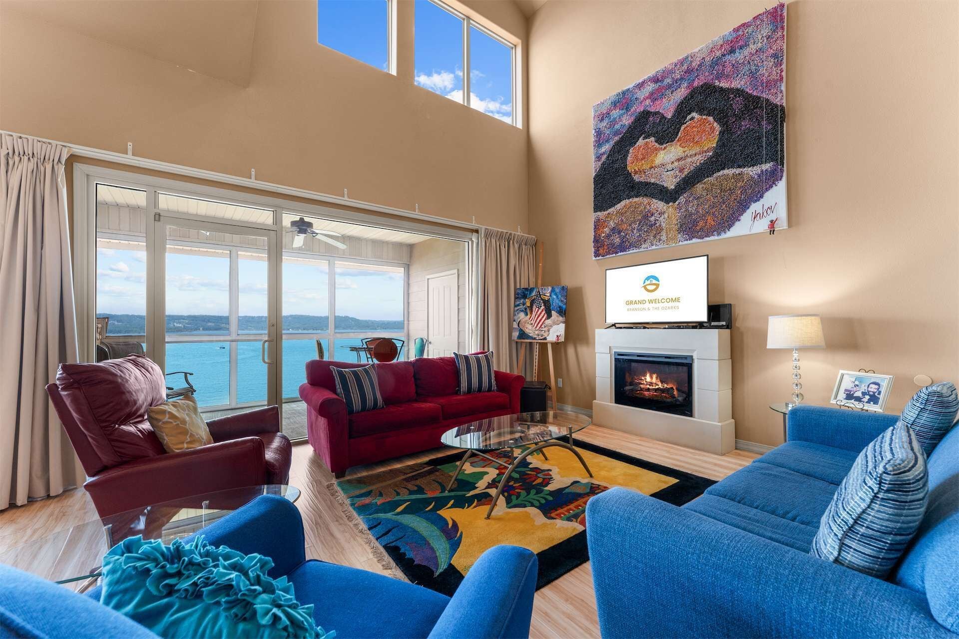 Ein ger äumiges Wohnzimmer mit großem Fenster zum Meer, einem Kamin und einem Fernseher, der eine Willkommensbotschaft zeigt.