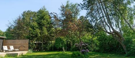 A backyard with a wooden deck, a tree with purple flowers, and a grassy lawn.