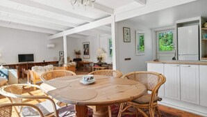 A spacious room with a round wooden table surrounded by wicker chairs, a chandelier, and white cabinetry. - 5 Star Holiday Home in Graested (Graested)