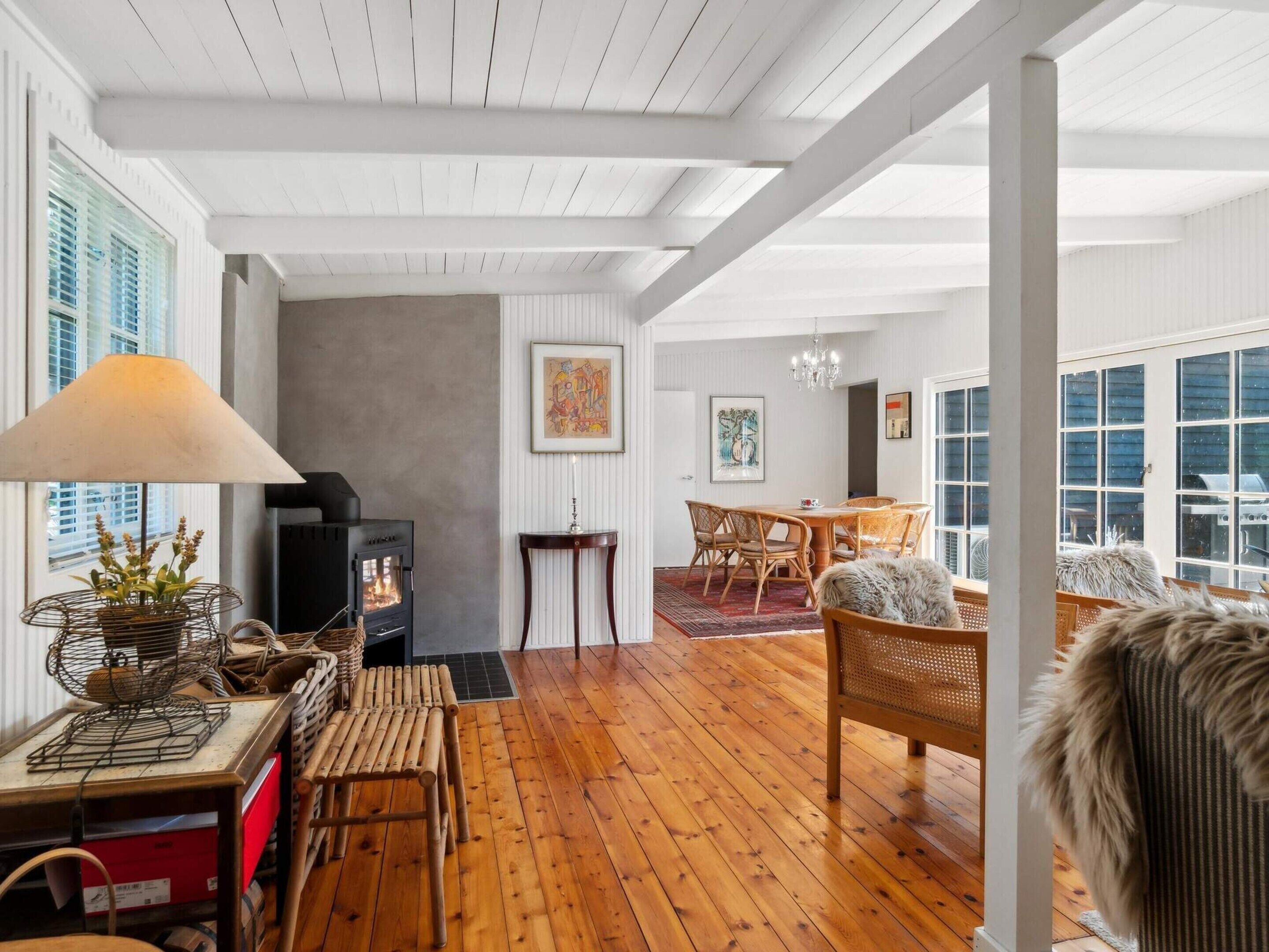 A spacious living area with a wooden floor, a fireplace, a dining table with chairs, and a large window providing a view outside.
