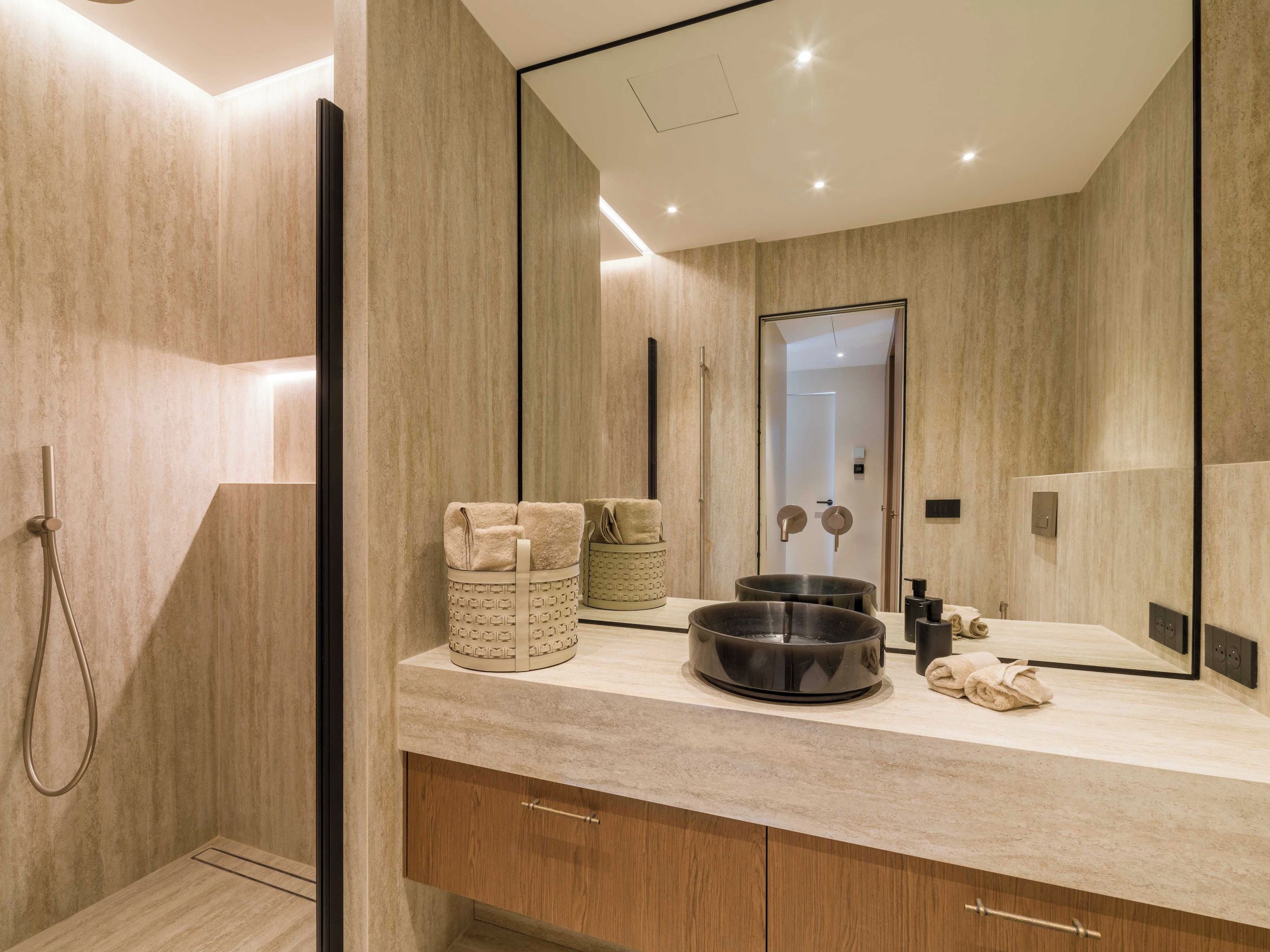 Un baño moderno con un espejo grande, ducha y tocador con lavamanos y espacio para toallas.