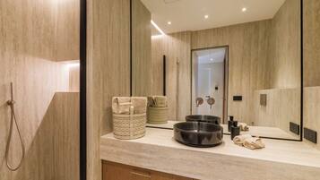 Un baño moderno con un espejo grande, ducha y tocador con lavamanos y espacio para toallas.