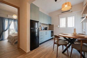 A modern kitchen with a refrigerator, stove, and dining area with chairs and a table. - Blue Nest Apartment by RentalsPro - Dionisiou Beach (Dionisiou Beach)