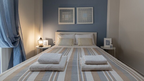 Habitación de hotel con una cama, dos mesitas de noche, una lámpara y una ventana con cortinas.