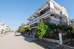 A multi-story residential building with balconies, a car parked on the street, and greenery along the sidewalk. - Blue Nest Apartment by RentalsPro - Dionisiou Beach (Dionisiou Beach)