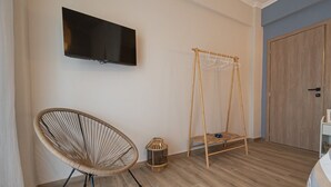 Una habitación con una televisión montada en la pared, una silla de mimbre, una cesta colgante pequeña y un armario de madera.