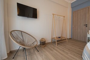 A room with a television mounted on the wall, a wicker chair, a small hanging basket, and a wooden wardrobe. - Blue Nest Apartment by RentalsPro - Dionisiou Beach (Dionisiou Beach)