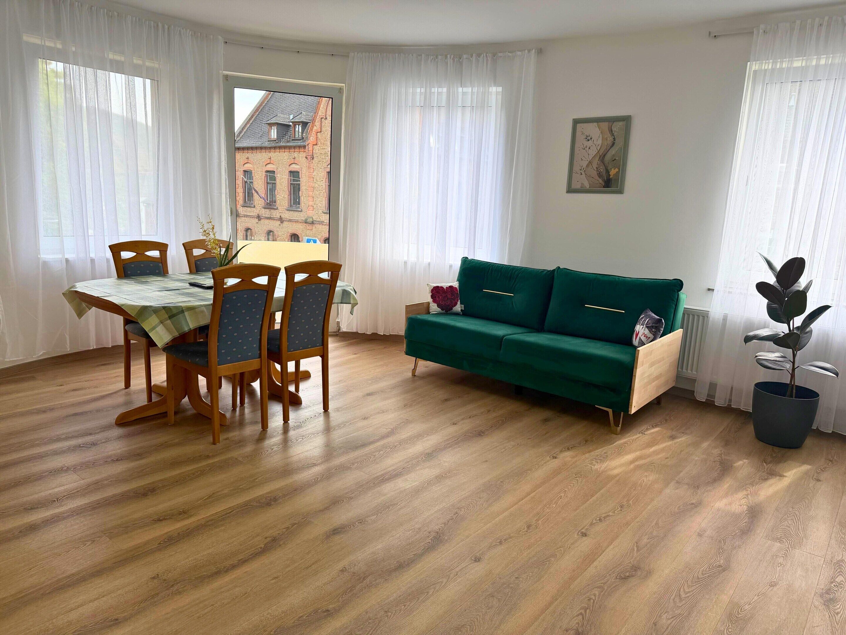 Ein Zimmer mit Esstisch, Stühlen, einer Couch und einer Topfpflanze.