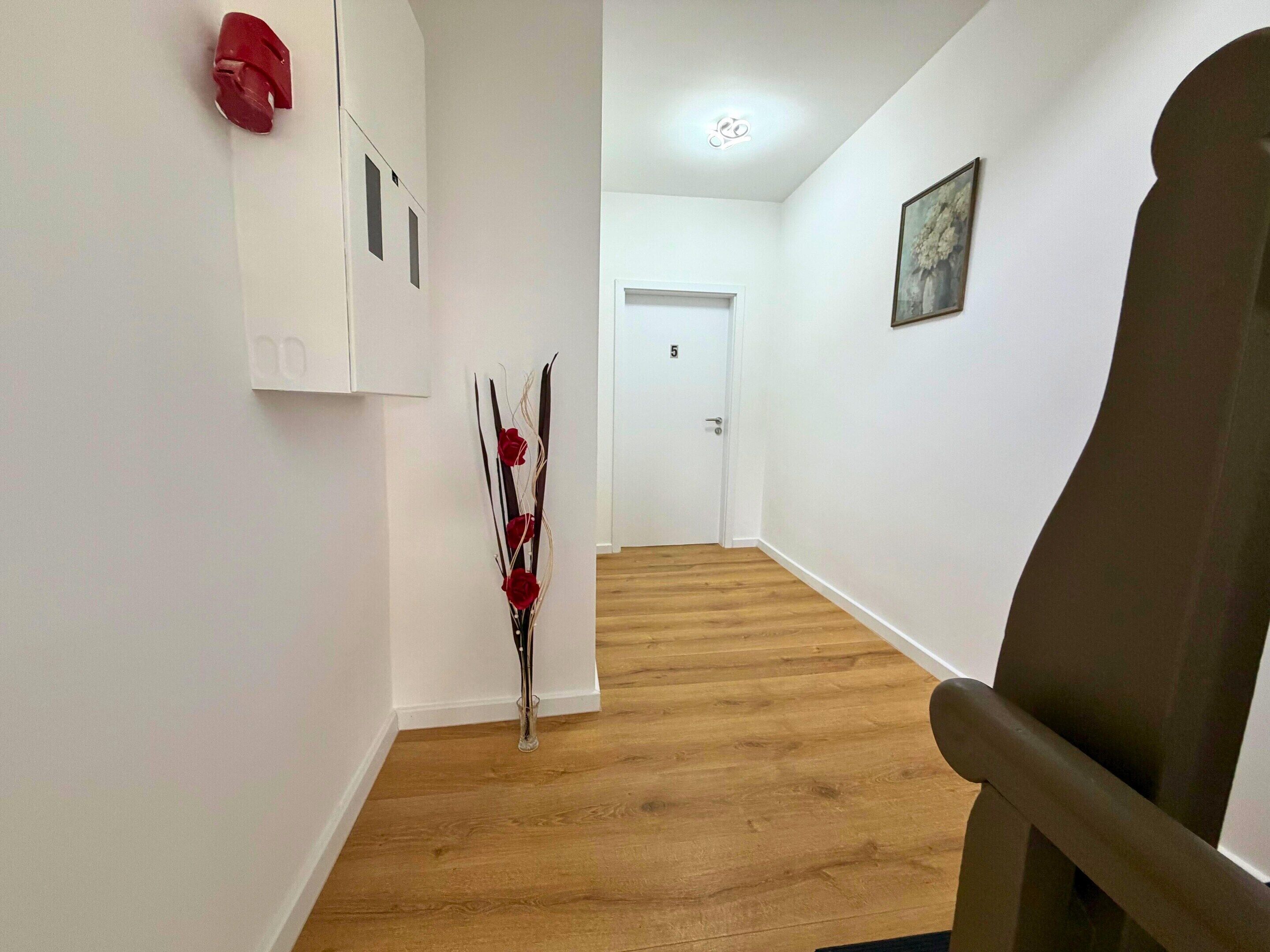 A hallway with a wooden floor, a door at the end, and a chair on the right.