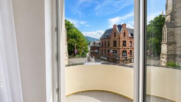 Blick von einem Balkon mit blauem Himmel, einem rotbackigen Gebäude und einer Steinstruktur im Hintergrund.