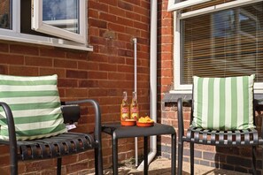 Two outdoor chairs with striped cushions, a small table with bottles and snacks, and a brick wall with windows. - Stylish 3BR, Warwick Hosp, Contractor long stays (Warwick)